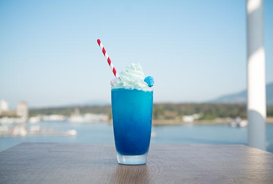 A blue slush drink with a red and white striped straw on a table.