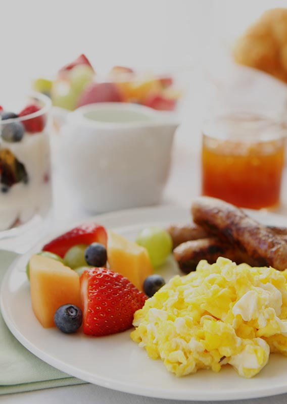 A breakfast plate with scrambled eggs, breakfast sausages and sliced fresh fruit.